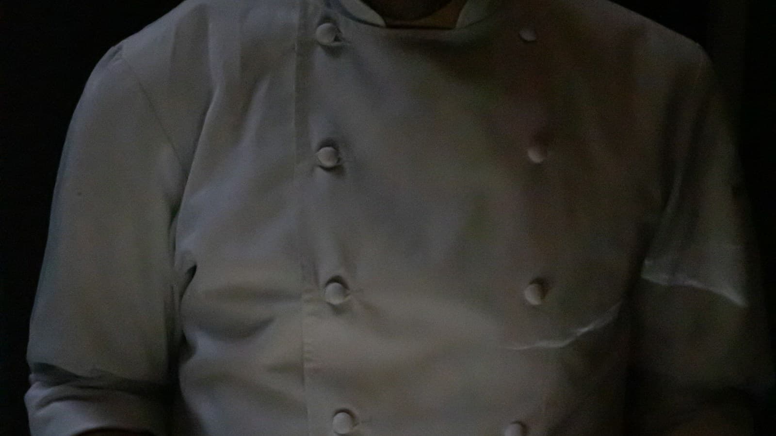 Chef presenting an artfully plated dish in a dark fine-dining room