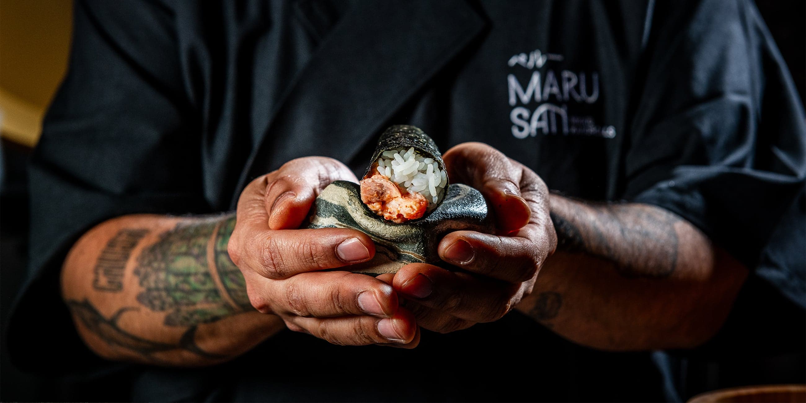 A moody restaurant counter with chefs plating dishes in a compact dining room