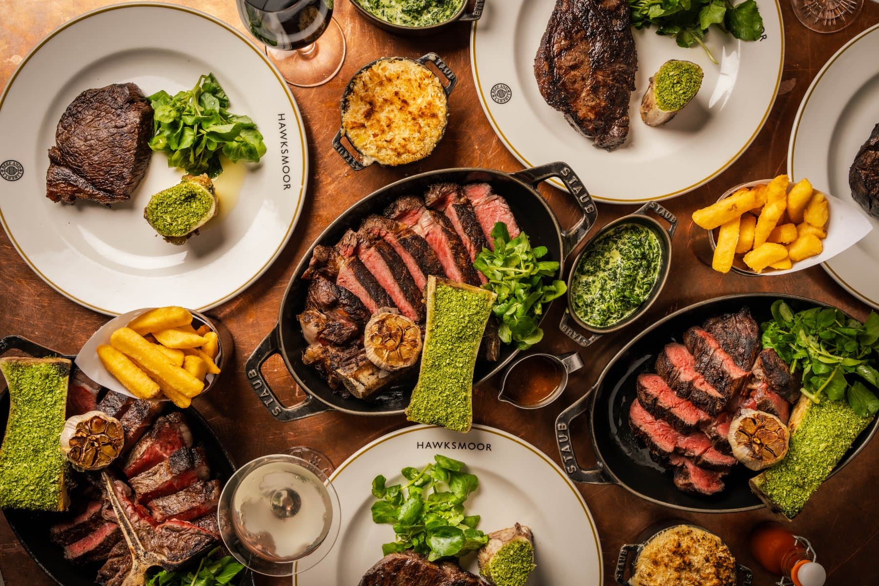 Steaks, seafood, and side dishes covering a Hawksmoor Boston dining table