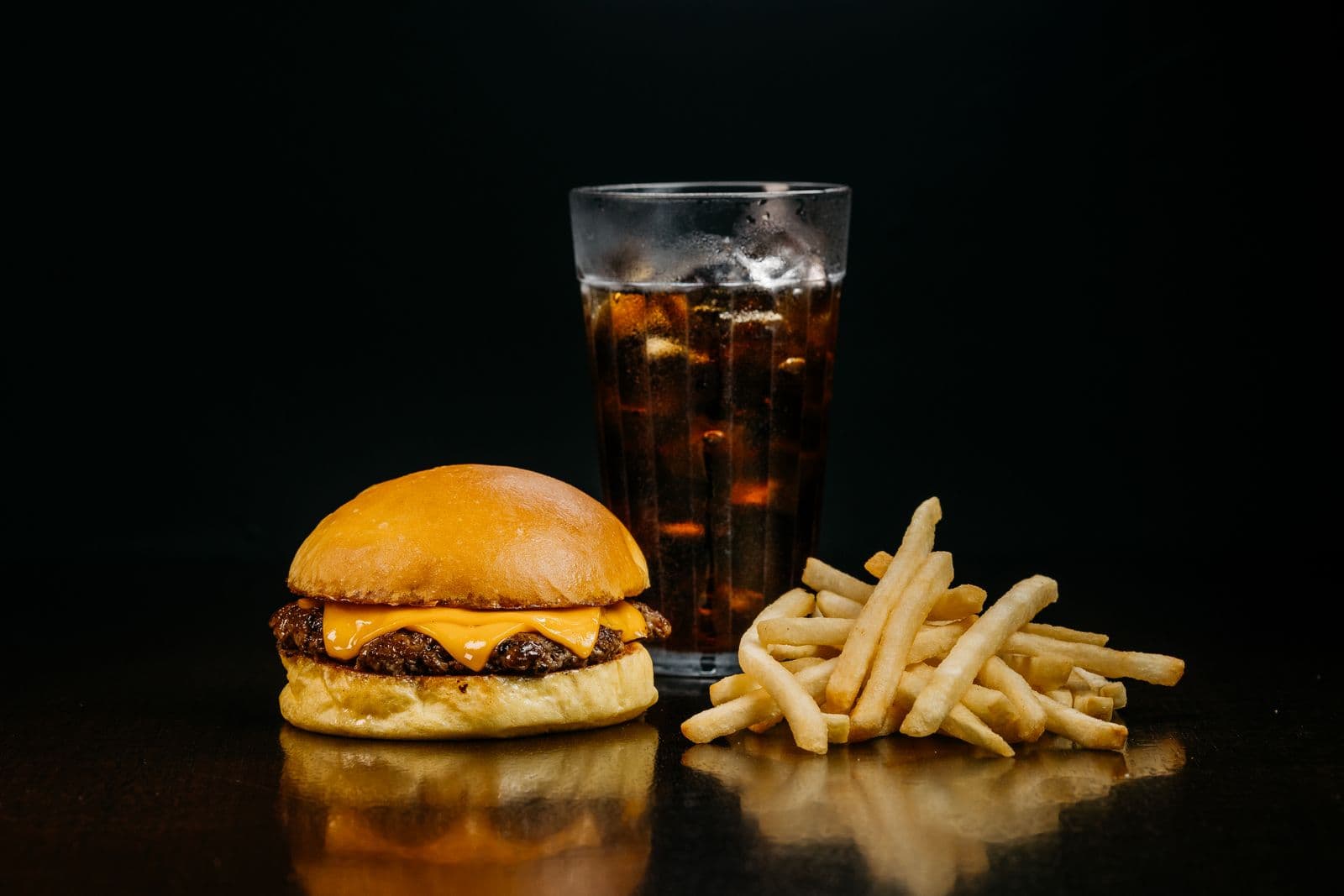 Cheeseburger, fries, and cola served against a dark restaurant backdrop