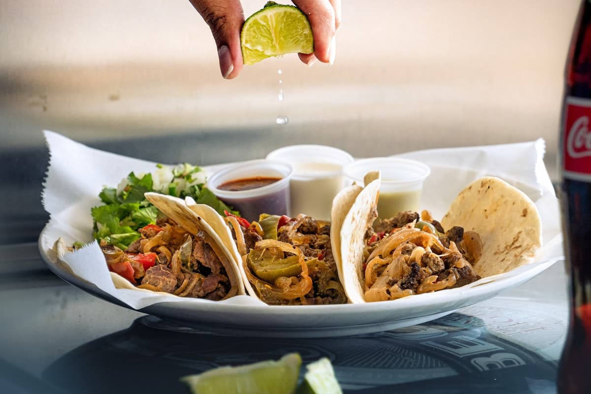 Close-up of tacos with lime, salsa, and charred meat on a warm restaurant table